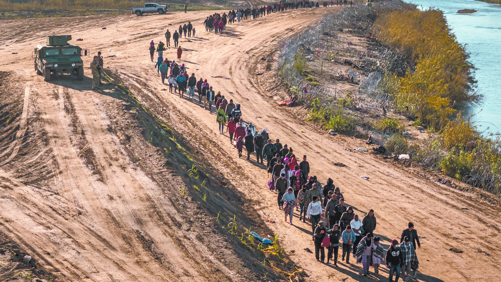 EAGLE PASS, TEXAS - DECEMBER 18: In this aerial view, A group of more than 1,000 immigrants walks towards a U.S. Border Patrol field processing center after they crossed the Rio Grande from Mexico on December 18, 2023 in Eagle Pass, Texas. A surge as many as 12,000 immigrants per day crossing the U.S. southern border has overwhelmed U.S. immigration authorities in recent weeks.   John Moore/Getty Images/AFP (Photo by JOHN MOORE / GETTY IMAGES NORTH AMERICA / Getty Images via AFP)