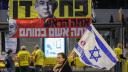 Una manifestante levanta una bandera israelí mientras pasa junto a una pancarta que representa al primer ministro israelí, Benjamin Netanyahu.