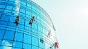 Industrial climbers cleaning blue windows outside building.
