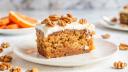 A slice of carrot cake with cream cheese frosting and pecans on a white plate.
