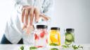 Hand takes one of rustic jars with cold fresh homemade lemonades from strawberry, orange, cucumber, ice and mint Close focus on first jar, action move, summer mood