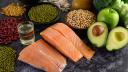 Legumes, broccoli, fruit, and salmon placed on a black cement floor. Top view.