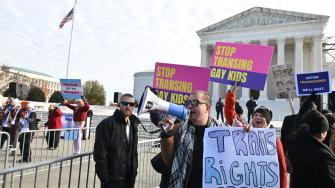 Varias personas sostienen carteles frente a la Corte Suprema de Estados Unidos durante los alegatos orales sobre si los estados pueden prohibir ciertos tratamientos médicos de transición de género para jóvenes.