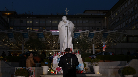 La gente se reúne cerca de la estatua del difunto Papa Juan Pablo II, afuera del Hospital Gemelli, donde el Papa Francisco está ingresado para recibir tratamiento, en Roma, Italia.