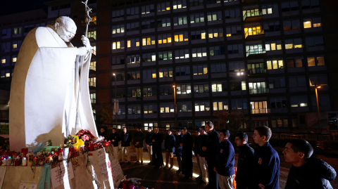La gente reza junto a la estatua del difunto Papa Juan Pablo II en el Hospital Gemelli, donde el Papa Francisco está ingresado para recibir tratamiento de neumonía, en Roma, Italia.