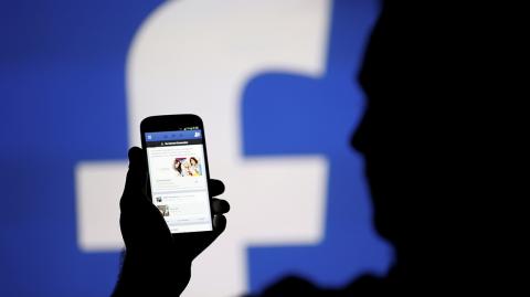 FILE PHOTO: A man is silhouetted against a video screen with an Facebook logo as he poses with an Samsung S4 smartphone in this photo illustration taken in the central Bosnian town of Zenica - FILE PHOTO: A man is silhouetted against a video screen with an Facebook logo as he poses with an Samsung S4 smartphone in this photo illustration August 14, 2013. REUTERS/Dado Ruvic/File Photo - NARCH/NARCH30