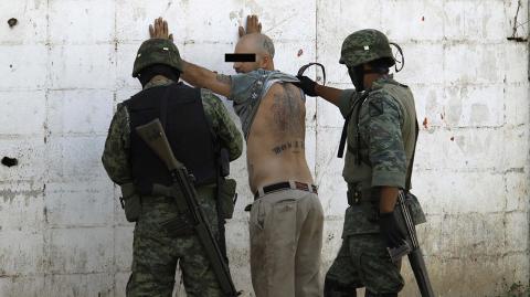 Soldiers frisk a man on suspicion of drugs and weapons at the site of a shooting in Guadalupe