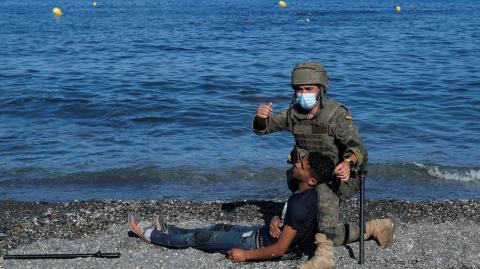 Un soldado español ayuda a un ciudadano marroquí en la playa El Tarajal, cerca de la valla entre la frontera hispano-marroquí, después de que miles de migrantes cruzaran esta frontera durante los últimos días, en Ceuta. Foto: Reuters.