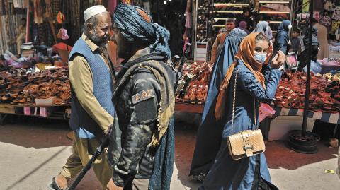 TOPSHOT - A Taliban fighter (C) walks past shoppers along Mandawi market in Kabul on September 1, 2021 a day after the US pulled all its troops out of the country to end a brutal 20-year war -- one that started and ended with the hardline Islamist in power. (Photo by HOSHANG HASHIMI / AFP)