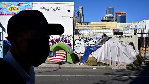 Un hombre pasa junto a tiendas de campaña que albergan a personas sin hogar. Foto: AFP.