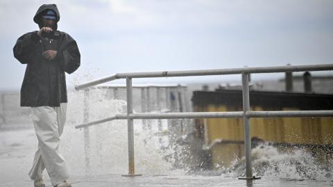 Un hombre usa su teléfono mientras las olas rompen contra la costa antes de la llegada del huracán Helene en Cedar Key, Florida.