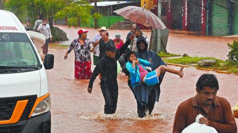 People walk on a flooded street after the hit of Hurricane John in Acapulco, Mexico, on September 26, 2024. - Hurricane John, which made landfall in Mexico on September 23, leaving at least five dead, re-formed as a cyclone early September 26, and is expected to hit the country again, authorities said. (Photo by Francisco Robles / AFP)