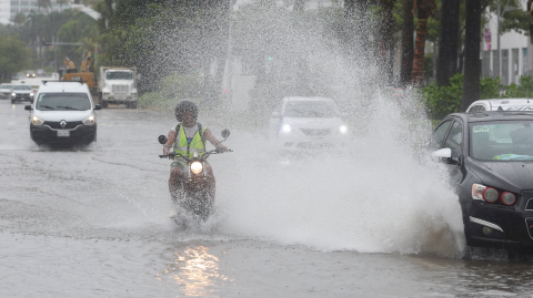 Un motociclista es sorprendido por un automovilista que circula por una calle inundada. tras el paso del huracán John en Acapulco