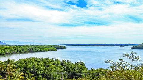 Cuyutlan Lagoon with its calm waters surrounded by green vegetation, blue sky with abundant white clouds in the background, tropical spring day in Manzanillo, Colima Mexico