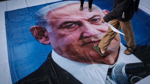 A demonstrator walks on a banner with a portrait of Israel's Prime Minister Benjamin Netanyahu during a pro-Palestinian rally on the eve of the first anniversary of the Israel-Hamas conflict, in Jakarta on October 6, 2024. (Photo by Yasuyoshi CHIBA / AFP)