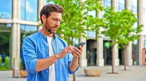 A young man businessman, freelancer stands near an office building and uses a mobile phone.