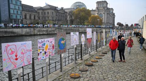 La gente avanza junto a una instalación al aire libre con carteles y carteles a lo largo del camino del antiguo Muro de Berlín en el 35º aniversario de la caída del Muro en Berlín, Alemania.