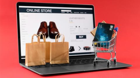 Online store. Laptop, small shopping cart, purchases and credit card on red background