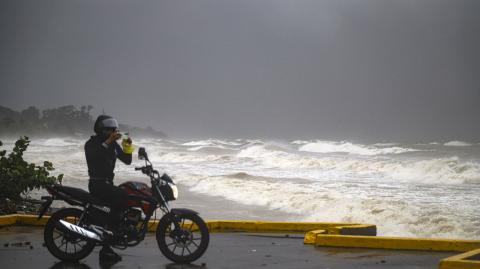 A motorcyclist takes photos at the boardwalk during the passage of tropical storm Sara in La Ceiba, Honduras, on November 15, 2024. - Honduras' President Xiomara Castro said emergency services had been activated to deal with "damage already caused by the rains," warning that Sara's impacts "could become a catastrophic event." (Photo by ESAU OCAMPO / AFP)