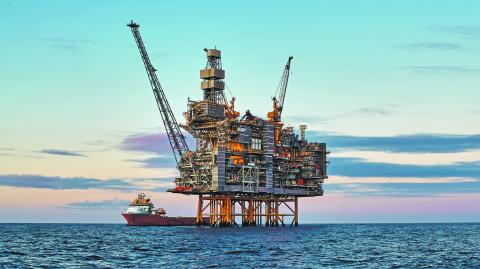 Offshore oil and gas jackup platform, during cargo operations with supply vessel in the sea and beautiful colourful sunset sky.