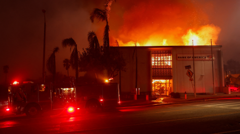 Humo y llamas se elevan desde un edificio del Bank of America, mientras los vientos que alimentan los devastadores incendios forestales en el área de Los Ángeles obligan a la gente a evacuar, en Eaton, en Altadena, California.