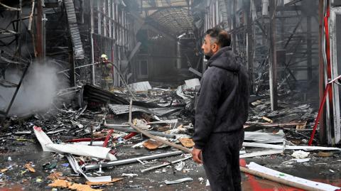Un hombre observa a un bombero ucraniano terminando de apagar un incendio en el mercado de Barabashovo tras un ataque con drones en Járkov.
