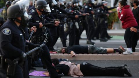 Policías antidisturbios avanzan entre manifestantes que se encuentran tendidos en la calle frente a la Oficina Local del Servicio de Ciudadanía e Inmigración de EU.