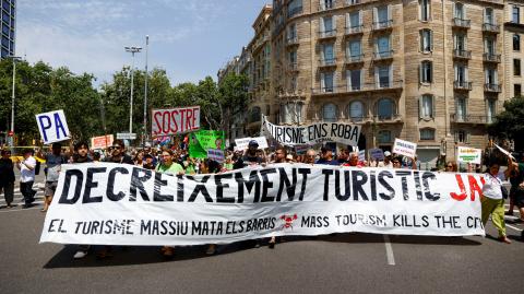 Personas sostienen una pancarta que dice "Disminuir el turismo ya" durante una protesta contra el turismo masivo, en Barcelona, España.