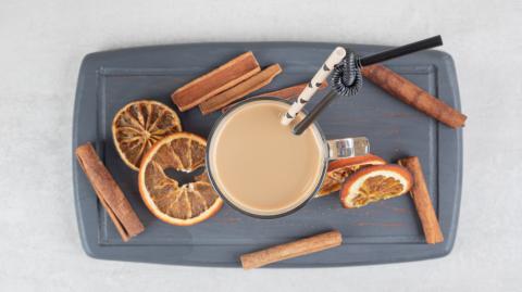 Tasty coffee, cinnamon sticks and orange slices on dark plate. High quality photo