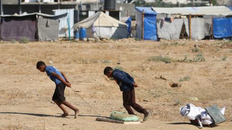Niños palestinos arrastran bolsas con objetos rescatados de un vertedero de basura en el campamento de Al-Bureij.