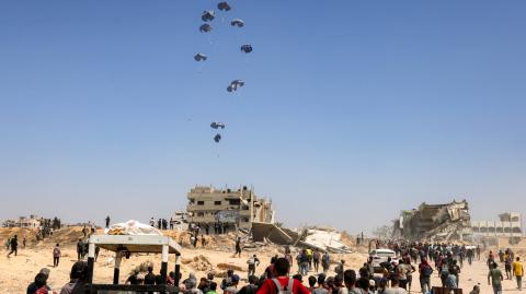 La gente se reúne mientras un avión de transporte militar C-130 Hércules lanza ayuda humanitaria sobre el norte de la Franja de Gaza el 27 de julio de 2025.