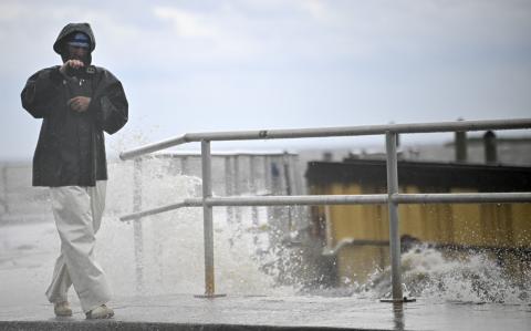 Un hombre usa su teléfono mientras las olas rompen contra la costa antes de la llegada del huracán Helene en Cedar Key, Florida.