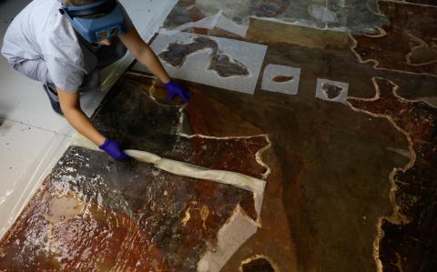 Un técnico de conservación y restauración retira la emulsión de disolvente gelificado durante el proceso de biolimpieza de un panel con una pintura mural retirada de la iglesia de Santos Juanes.