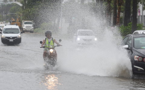 Un motociclista es sorprendido por un automovilista que circula por una calle inundada. tras el paso del huracán John en Acapulco