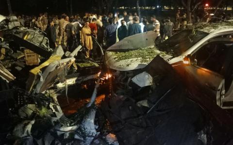 La gente se encuentra cerca de los restos de los vehículos mientras se reúnen después de una explosión cerca del Aeropuerto Internacional Yiná en Karachi.