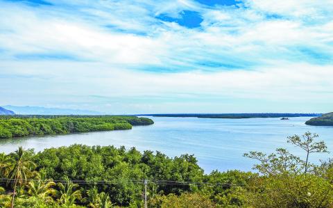 Cuyutlan Lagoon with its calm waters surrounded by green vegetation, blue sky with abundant white clouds in the background, tropical spring day in Manzanillo, Colima Mexico