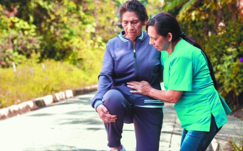 A nurse helps an elderly woman stay active and healthy with outdoor physical therapy stretches.