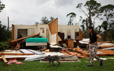 Una mujer pasea a un perro junto a una casa dañada tras la llegada del huracán Milton, en Lakewood Park, cerca de Fort Pierce, en el condado de St. Lucie, Florida.