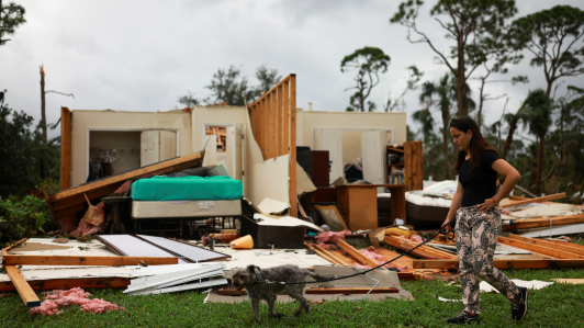 Una mujer pasea a un perro junto a una casa dañada tras la llegada del huracán Milton, en Lakewood Park, cerca de Fort Pierce, en el condado de St. Lucie, Florida.