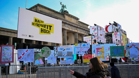 La gente avanza junto a una instalación al aire libre con carteles y carteles a lo largo del camino del antiguo Muro de Berlín en el 35º aniversario de la caída del Muro en Berlín, Alemania.