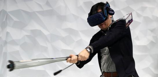 Un hombre practica béisbol usando un dispositivo VR dentro de la cabina de HTC, en el MWC 2019.