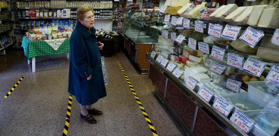 Una mujer espera ser atendida detrás de las líneas amarillas que marcan la distancia que los clientes deben mantener entre ellos dentro de una tienda de comestibles en Roma, Italia.