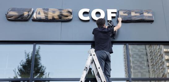 Un miembro del personal quita una cubierta de un letrero de la nueva cafetería "Stars Coffee" que se abre en Moscú.