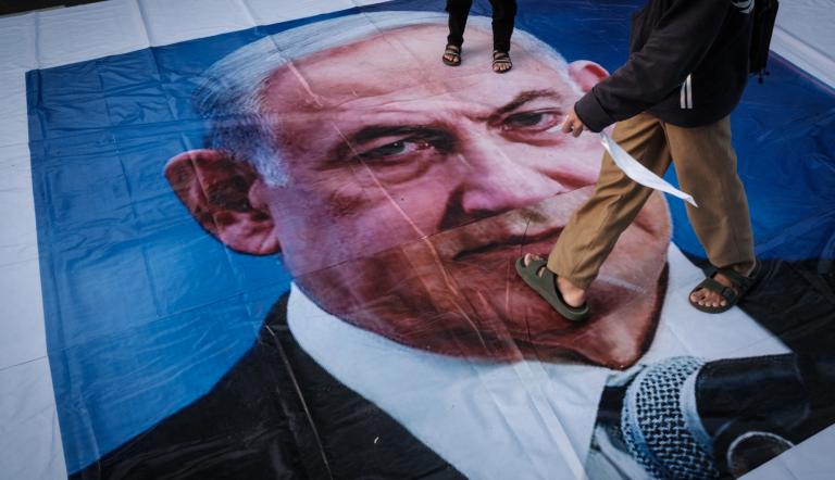 A demonstrator walks on a banner with a portrait of Israel's Prime Minister Benjamin Netanyahu during a pro-Palestinian rally on the eve of the first anniversary of the Israel-Hamas conflict, in Jakarta on October 6, 2024. (Photo by Yasuyoshi CHIBA / AFP)