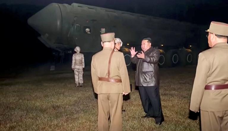 El líder norcoreano Kim Jong Un y funcionarios militares se encuentran junto a lo que dicen es un vehículo lanzamisiles móvil.