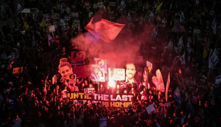 La gente enciende bengalas y sostiene pancartas durante una protesta antigubernamental que pide medidas para asegurar la liberación de los rehenes israelíes cautivos desde los ataques del 7 de octubre de 2023 perpetrados por militantes palestinos en la Franja de Gaza.