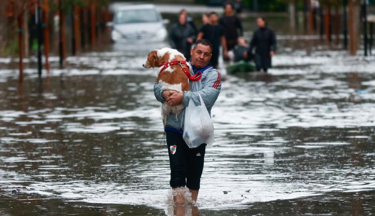 Un hombre lleva un perro mientras camina en medio de las inundaciones provocadas por las fuertes lluvias, en Capilla del Señor, en Buenos Aires.
