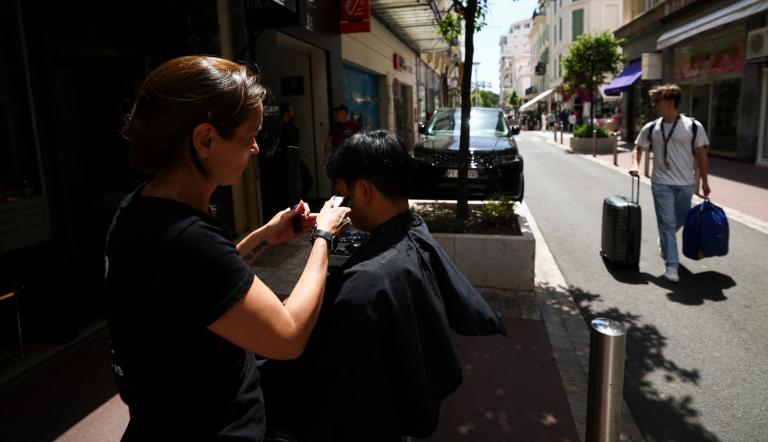Una peluquera corta el pelo a una clienta en la calle debido a la falta de luz en su peluquería, tras un importante apagón, durante el 78º Festival de Cine de Cannes.