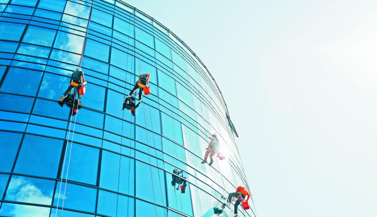 Industrial climbers cleaning blue windows outside building.