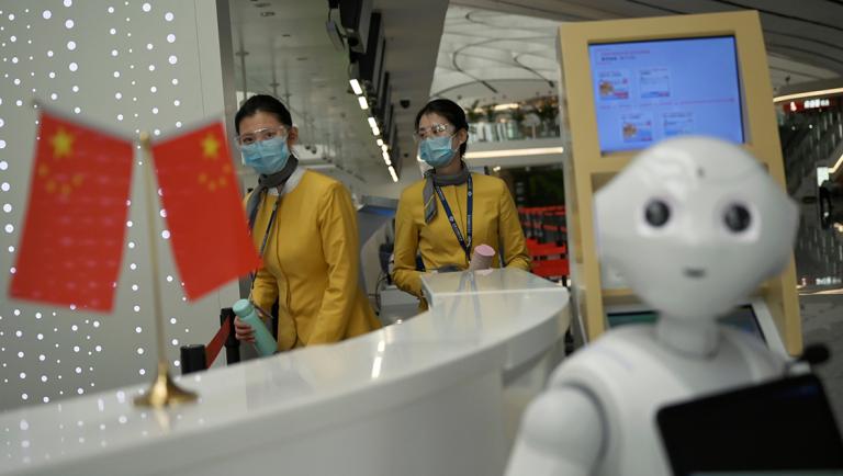 Staff members wearing face masks and goggles are seen near Chinese flags displayed at a counter at the Beijing Daxing International Airport